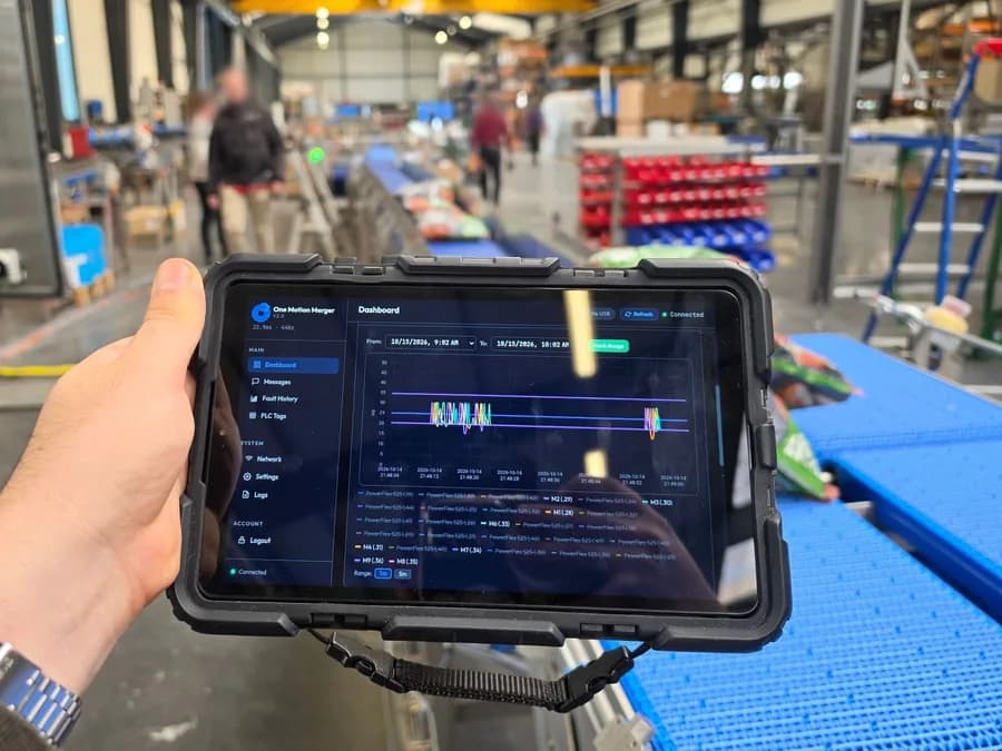 A hand holding a rugged tablet showing the Cortex dashboard, beside a blue conveyor on a factory floor